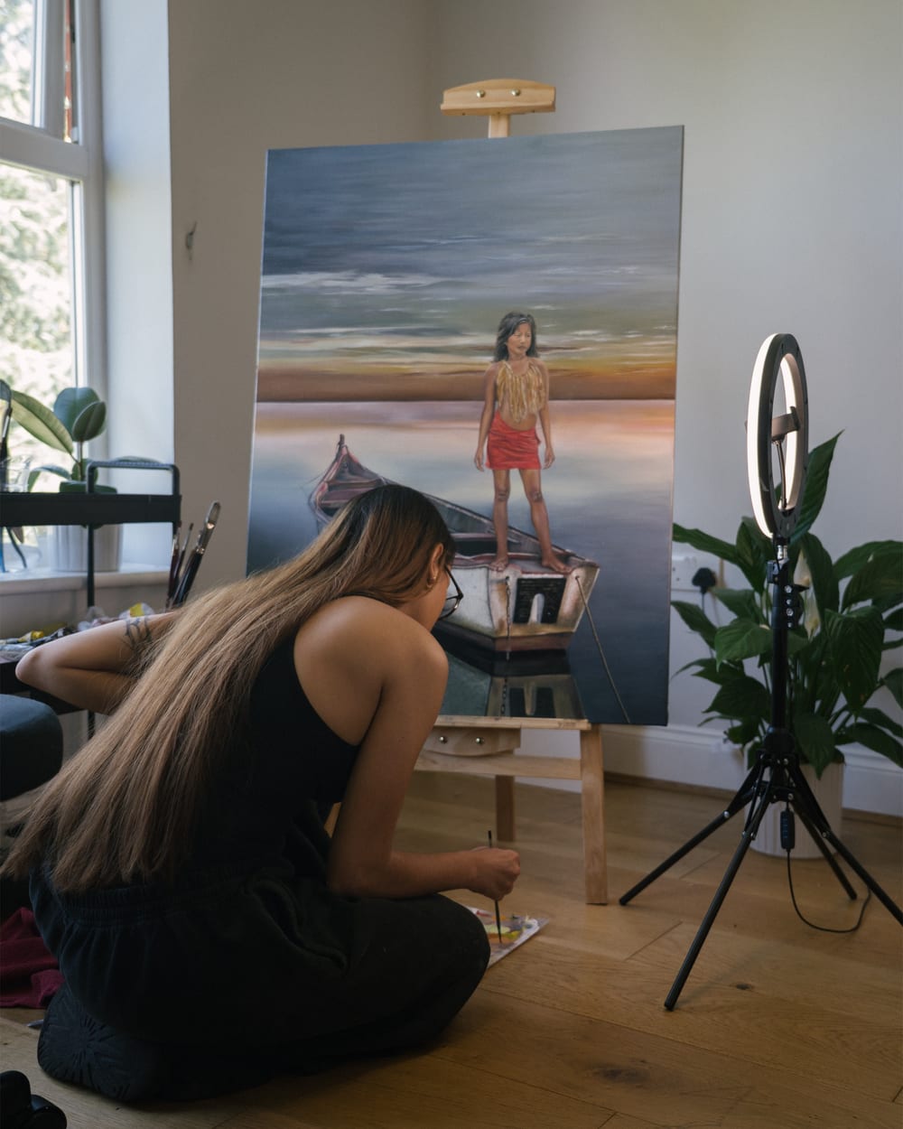 Valeria sitting on the floor of the studio, painting Guerrera on its easel.