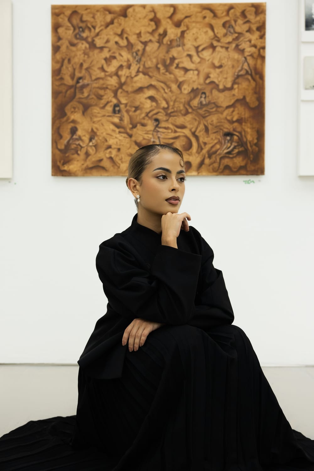 Valeria seated in front of Pachamama at Saatchi Gallery, hand to her chin.