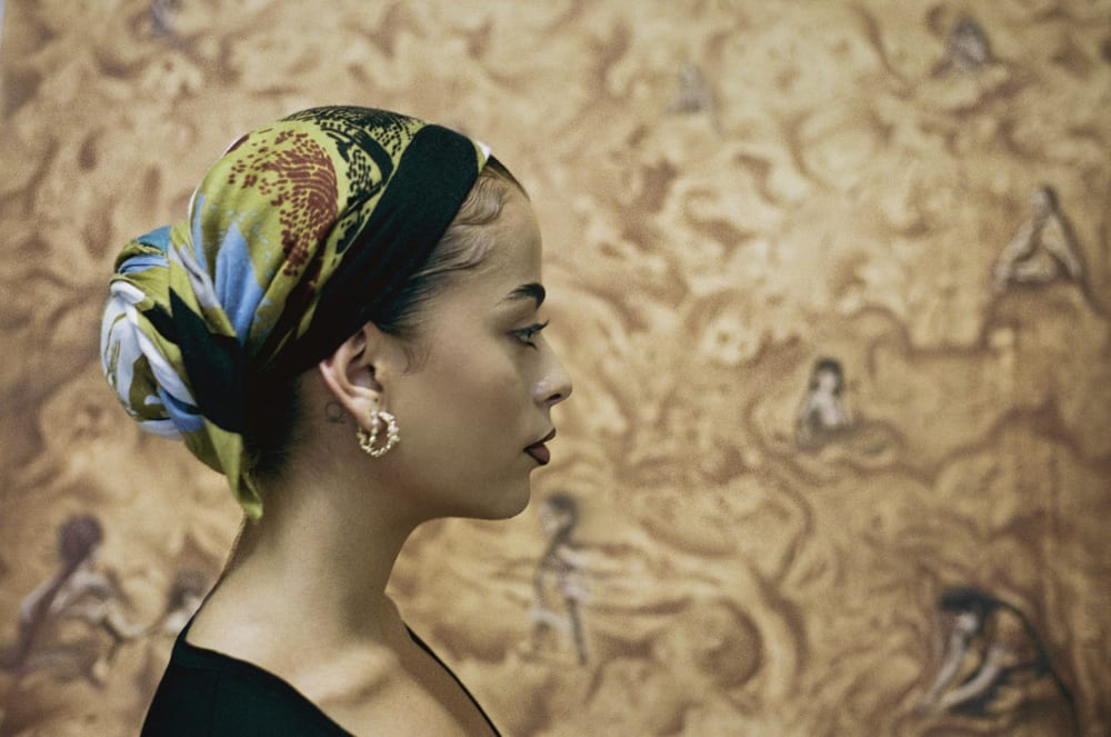 Valeria in profile in a patterned silk headscarf, Pachamama behind her.
