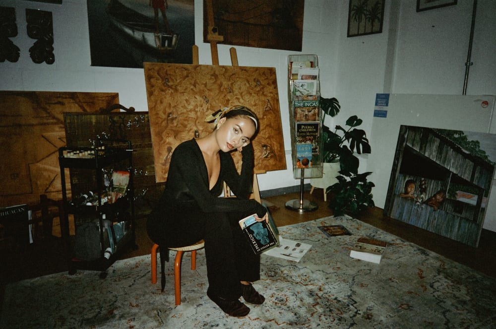 Valeria seated on a stool in the studio, Pachamama on the easel behind her.